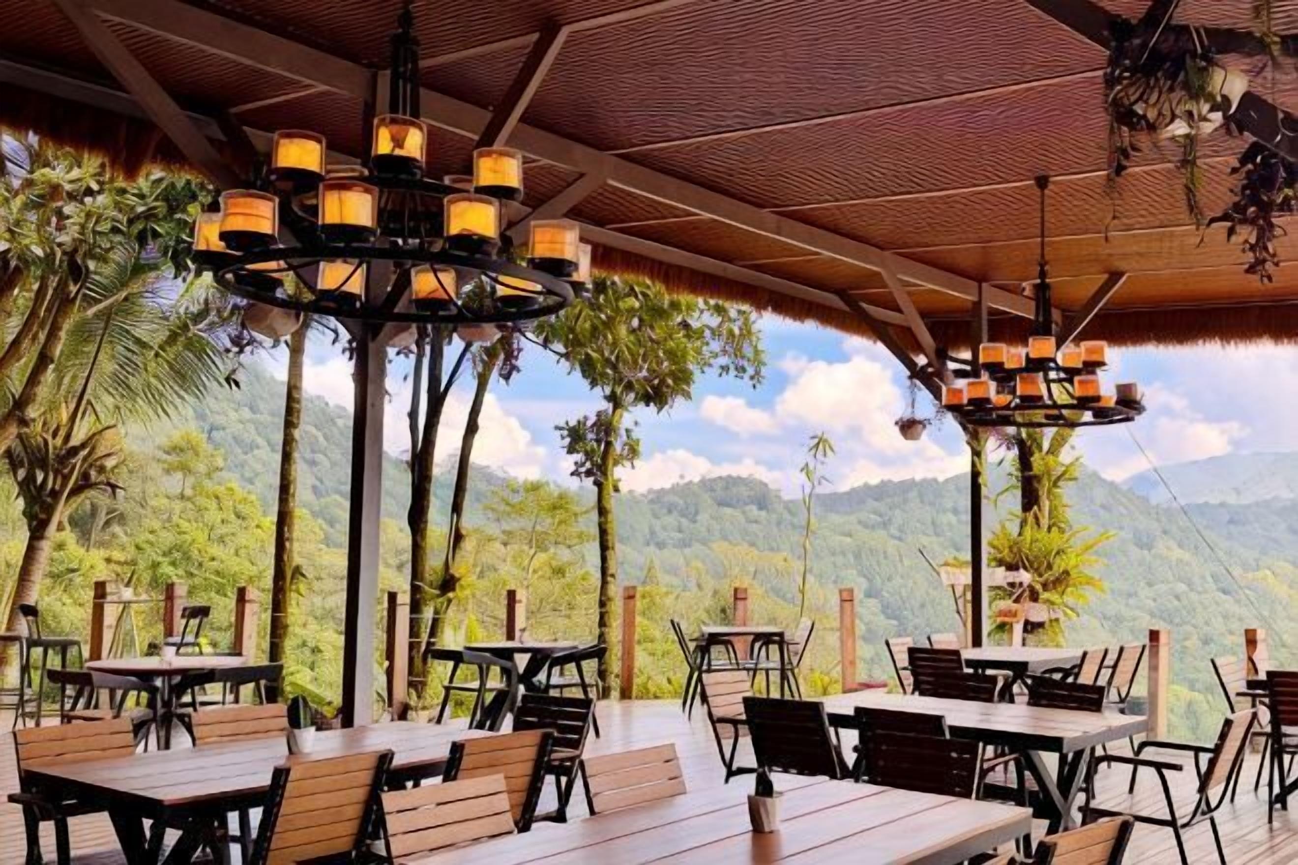 An outdoor dining area with tables and chairs, a wooden ceiling, and a view of mountains and trees.