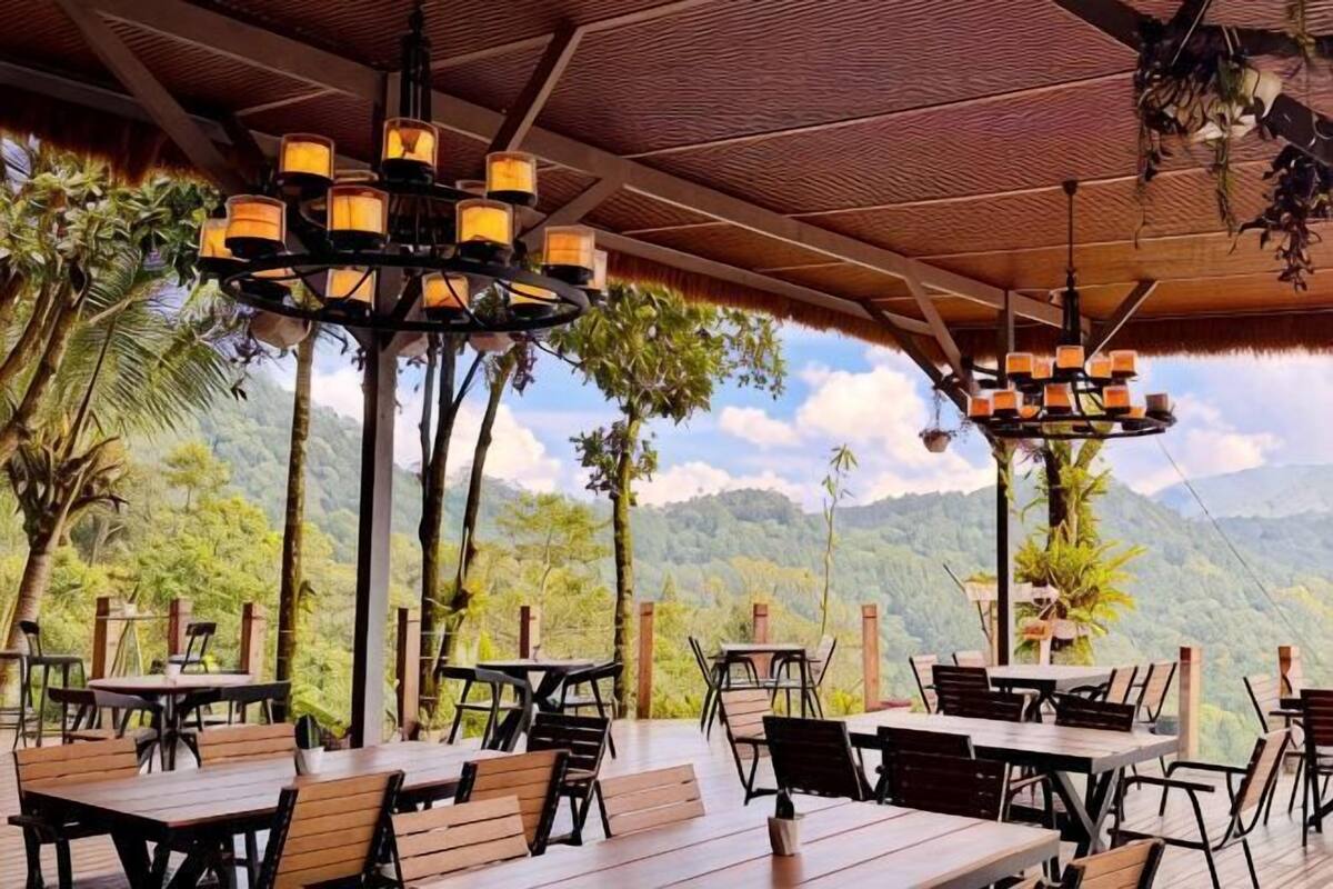 An outdoor dining area with tables and chairs, a wooden ceiling, and a view of mountains and trees.