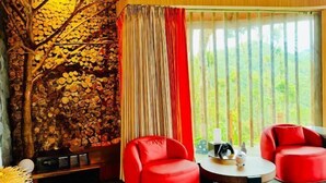 Quarto com parede de madeira, cadeiras vermelhas, uma mesa redonda e vista para o verde lá fora.