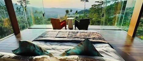 A bedroom with a large bed, a view of the outdoors, and a seating area with chairs.