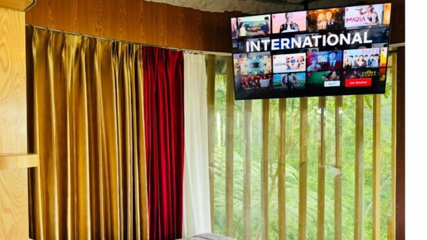 Quarto de hotel com cama, cortinas e televisão exibindo um canal internacional.