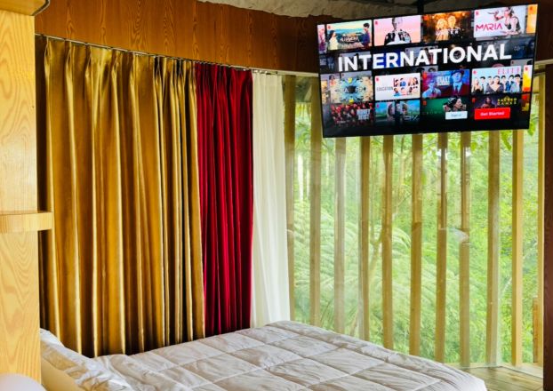 Une chambre d’hôtel avec un lit, des rideaux et un téléviseur diffusant une chaîne internationale.