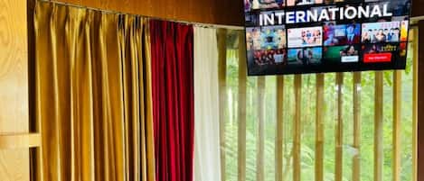 Une chambre d’hôtel avec un lit, des rideaux et un téléviseur diffusant une chaîne internationale.