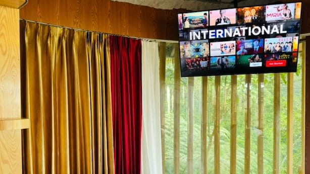 A hotel room with a bed, curtains, and a TV displaying an international channel. - Forest 101 (Real)
