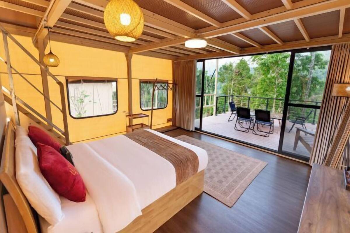 A bedroom with a bed, a window, a balcony with chairs, and a wooden ceiling.