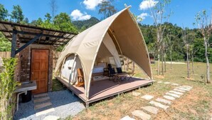 A tented accommodation with a wooden deck, a stone pathway, and a rustic building in the background. - Lu Ying Retreats (Bentong)