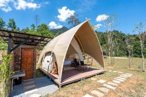 Un alojamiento en tienda de campaña con terraza de madera, un camino de piedra y un edificio rústico al fondo.