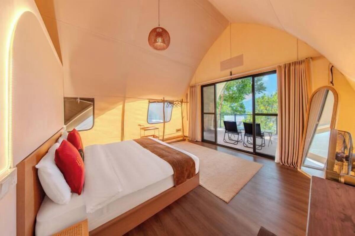 A spacious tent-style room with a large bed, a dining area, and a view of the outdoors.