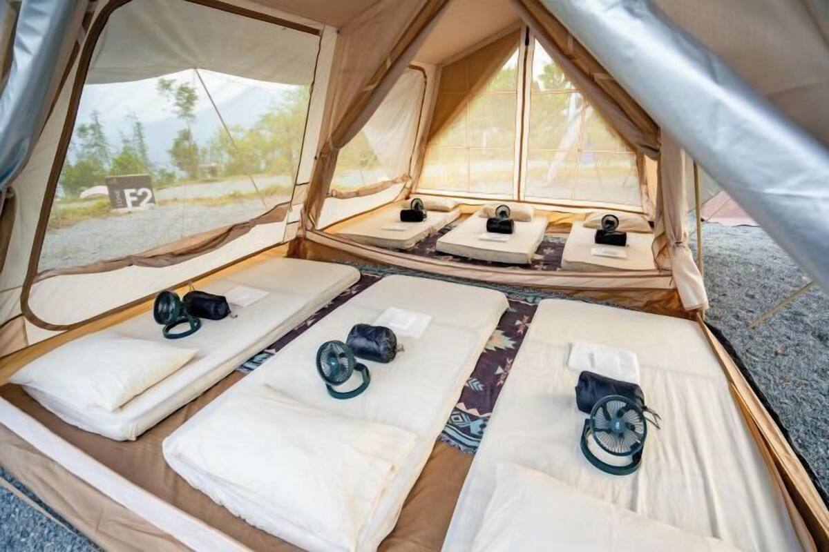 A tent with two beds, each with a pillow, a camera, and a fan.
