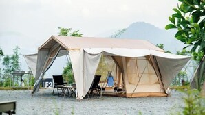 A tent with a table and chairs set up on a gravel surface, surrounded by greenery and a mountain in the background. - Lu Ying Retreats (Bentong)