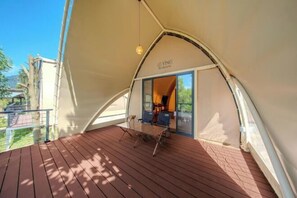 Una carpa con una mesa y sillas en el balcón, una lámpara colgante y una puerta que da al interior.