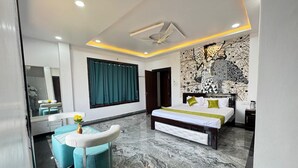 A modern bedroom with a large bed, a bench, and a seating area with a mirror and a vase of flowers. - Sathya Hotels & Resorts (Hyderabad)