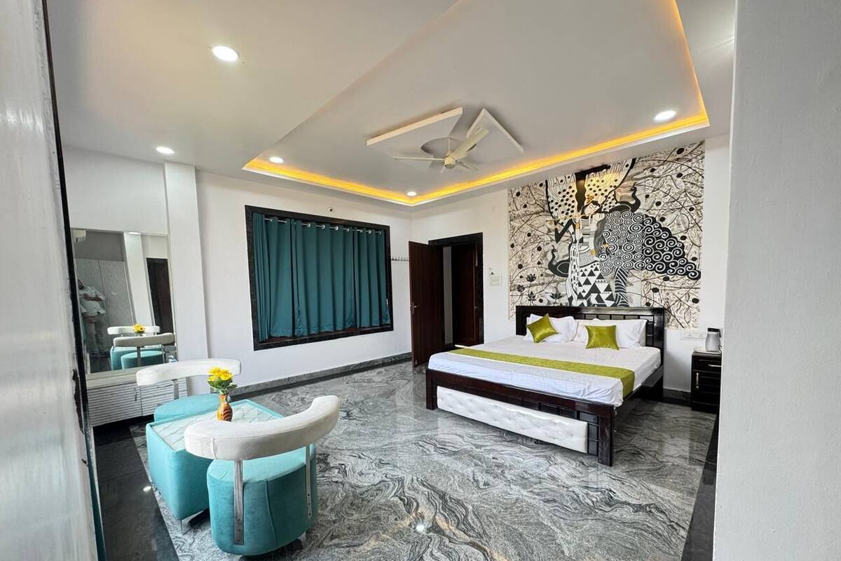 Un dormitorio moderno con una cama grande, un banco y una zona de estar con un espejo y un jarrón de flores.
