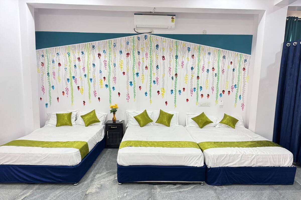Habitación de hotel con dos camas, cada una con una colcha verde y blanca, una mesita de noche con un jarrón de flores y un aire acondicionado de pared.