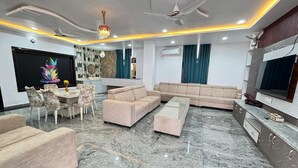 A modern living room with a marble floor, beige sofas, a dining table with chairs, a TV, and a ceiling fan. - Sathya Hotels & Resorts (Hyderabad)