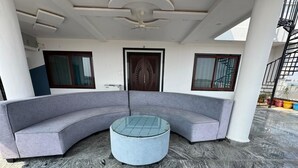 A curved grey sofa with a glass-top coffee table in a covered outdoor area with marble flooring. - Sathya Hotels & Resorts (Hyderabad)