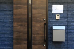 Una porta con maniglia e serratura, una piccola targa e un quadro elettrico su un muro in mattoni.