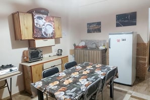 A compact kitchen with a microwave, toaster, and refrigerator. There is a dining table with chairs and a cabinet above it.