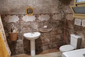 Ein Badezimmer mit einem weißen Waschbecken, einer Toilette, einem Spiegel und einer gefliesten Wand.