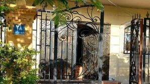 A wrought iron gate with intricate designs, a small potted plant, and a blue sign on the wall. - Jamila Residential Apartment (Cairo)