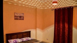 A bedroom with a bed, a window with curtains, a wall-mounted light fixture, and a small picture on the wall. - Jamila Residential Apartment (Cairo)