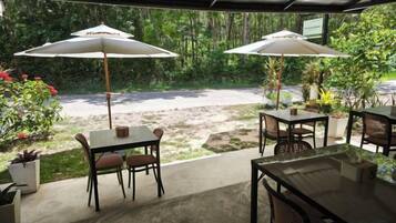 An outdoor patio area with tables and chairs, two umbrellas, and potted plants.