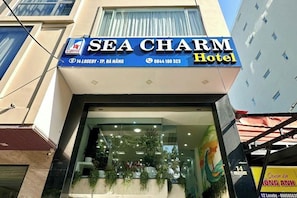 The exterior of the Sea Charm Hotel with a clear entrance, a signboard displaying the name and contact information, and a visible address. - Sea Charm Hotel (Da Nang)