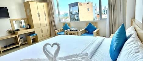 A hotel room with a bed, a desk, a chair, a TV, and a window with a city view.