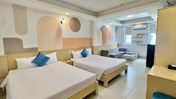 A hotel room with two beds, a sofa, a TV, and a desk. - Sea Charm Hotel (Da Nang)