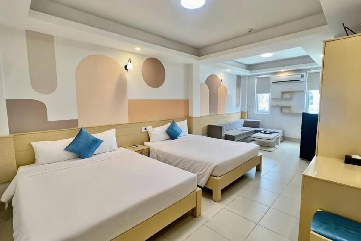 A hotel room with two beds, a sofa, a TV, and a desk.