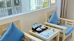 A hotel room with a glass-top table, two wooden chairs with blue cushions, and a tray with water bottles and a teapot. - Sea Charm Hotel (Da Nang)