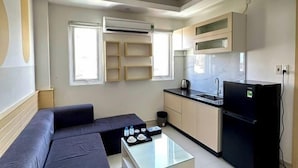 A compact living space with a sofa, a glass coffee table, a kitchen area with a refrigerator, and built-in shelves. - Sea Charm Hotel (Da Nang)