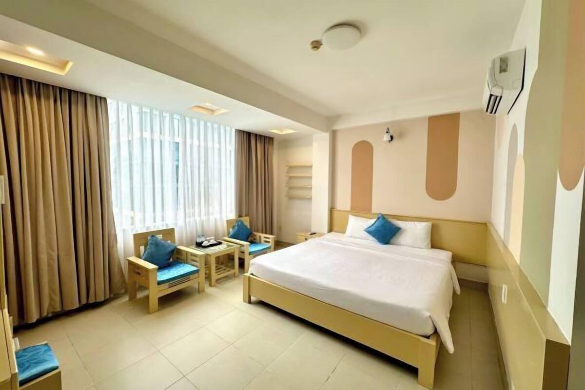 A hotel room with a large bed, a desk with a chair, and a window with curtains.