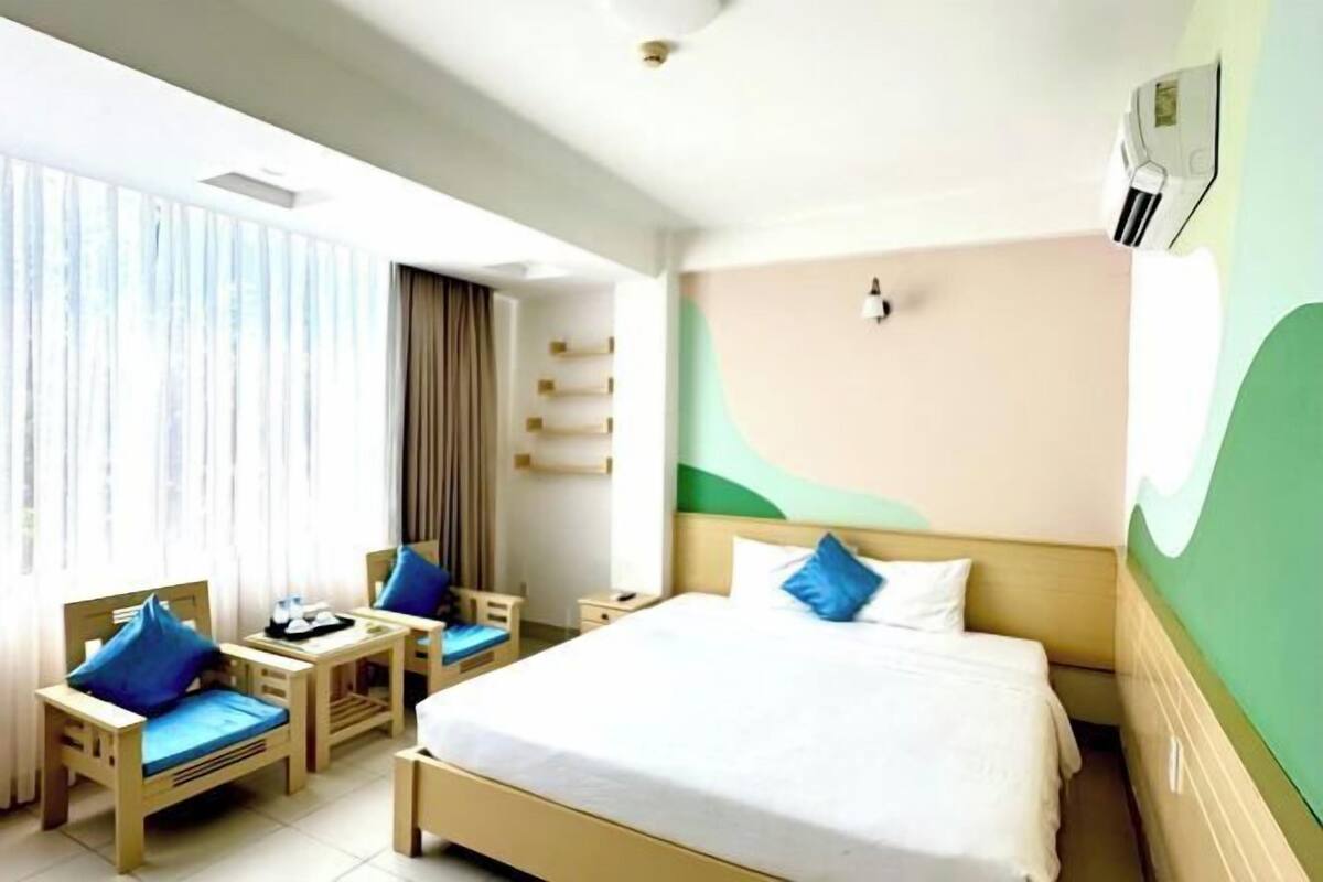 A hotel room with a bed, two chairs, a small table, and a window with curtains.