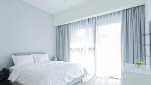 Un dormitorio moderno con cama, mesita de noche y un amplio ventanal con cortinas.