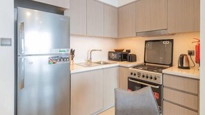 Una cocina compacta con refrigerador de acero inoxidable, microondas, estufa y pileta.