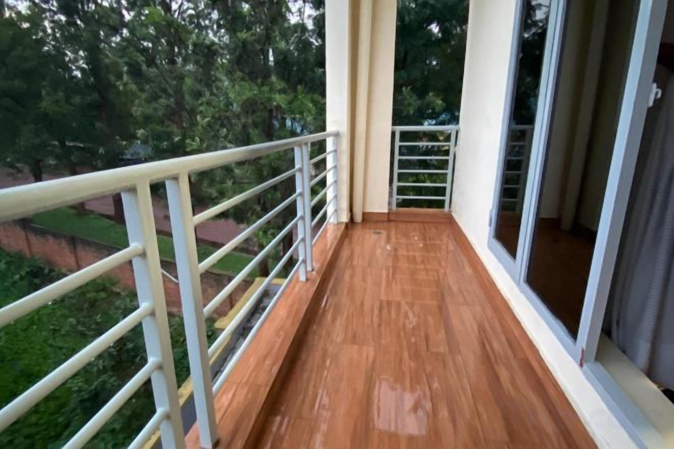 A balcony with a wooden floor and white railing, overlooking a green area.