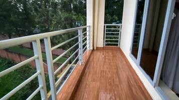 A balcony with a wooden floor and white railing, overlooking a green area.