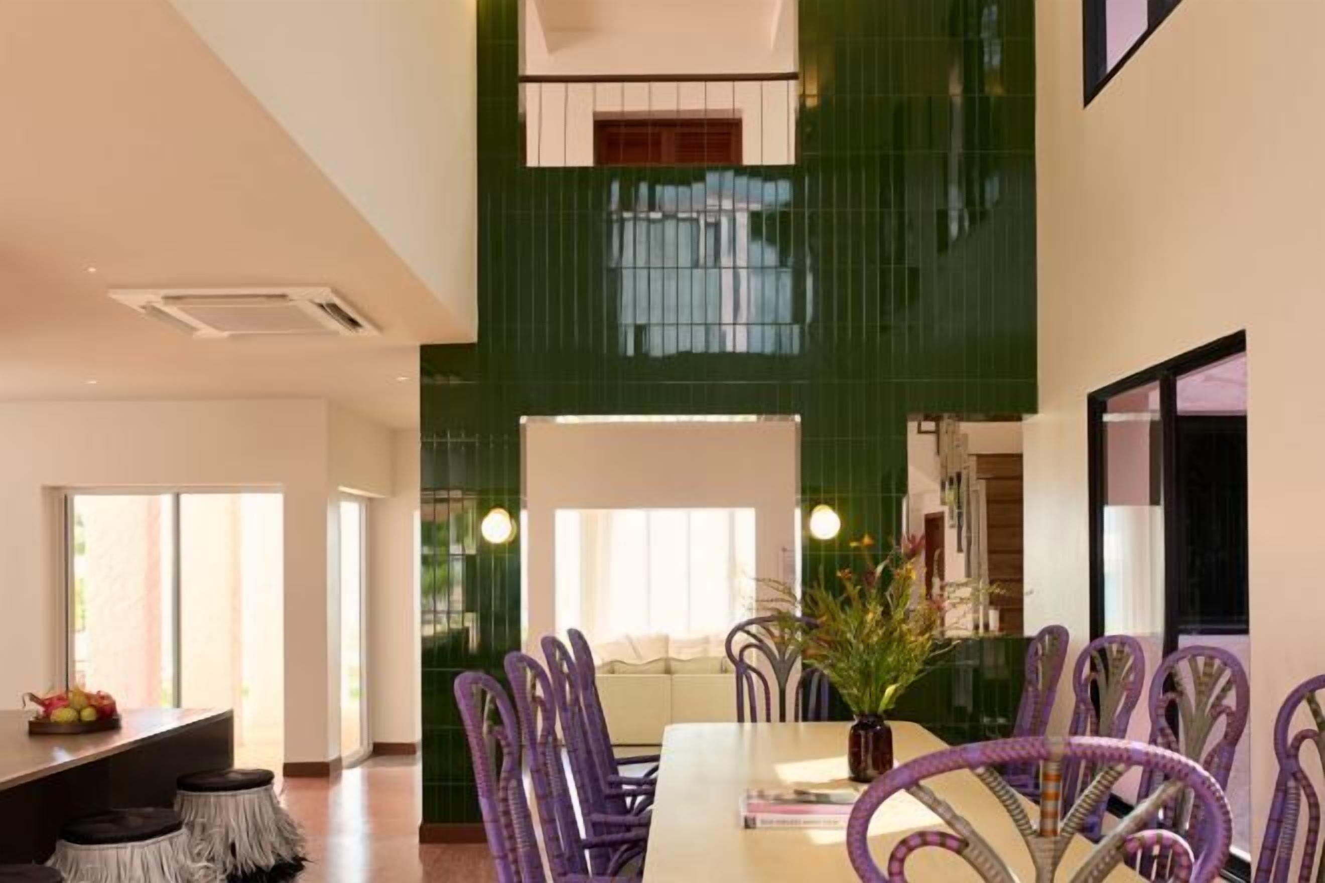 A dining area with a long table and purple chairs, a green accent wall, and a large window.