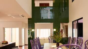 A dining area with a long table and purple chairs, a green accent wall, and a large window.