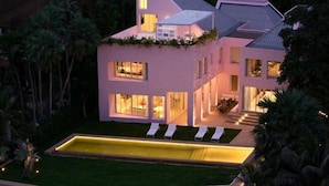 Una casa moderna con piscina, ventanas amplias y un exterior bien iluminado al anochecer.