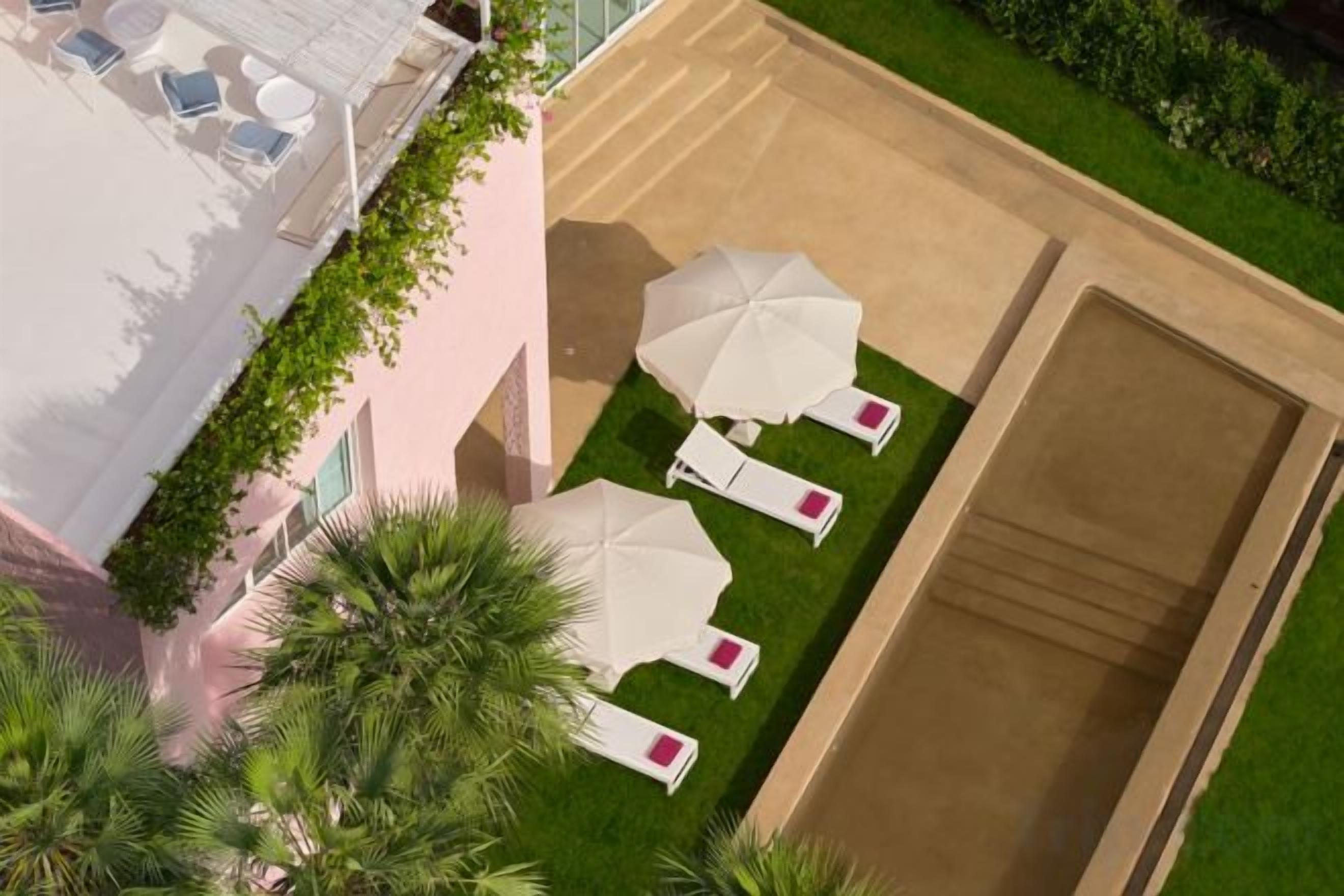 Vista aérea de un hotel con terraza en la azotea, palmeras y mobiliario exterior con sombrillas.
