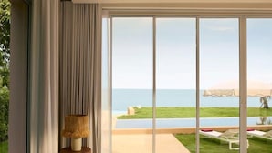 Un dormitorio con un amplio ventanal corredera que da a una zona de piscina con vistas al mar.