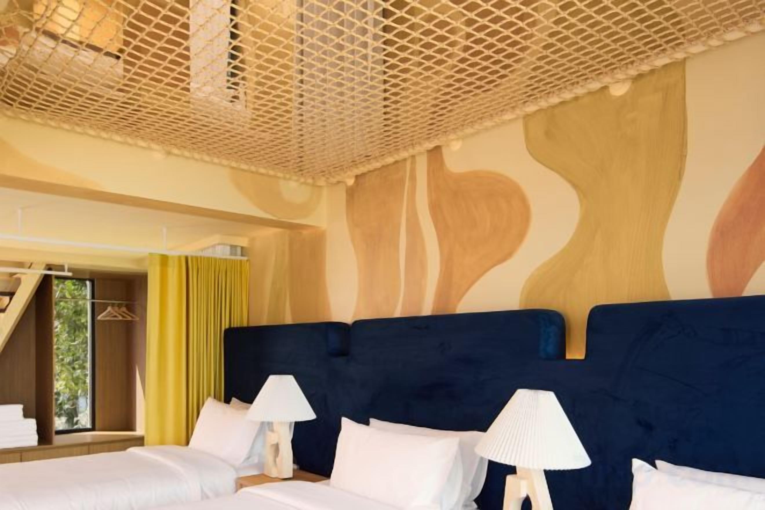 A hotel room with two beds, a large window, and a unique ceiling design.