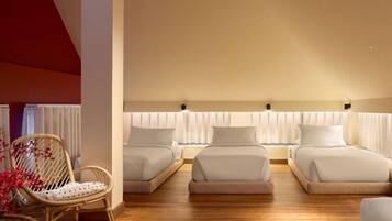 A hotel room with a high ceiling, three beds, a wicker chair, and a window with curtains.