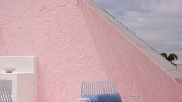 Pared rosa con textura, una repisa blanca y dos sillas blancas con cojines azules.