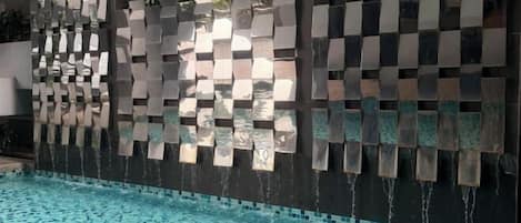 A pool area with a decorative wall featuring a waterfall feature.