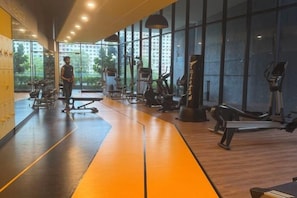 Een fitnessruimte met trainingsapparatuur, een spiegelwand en grote ramen.