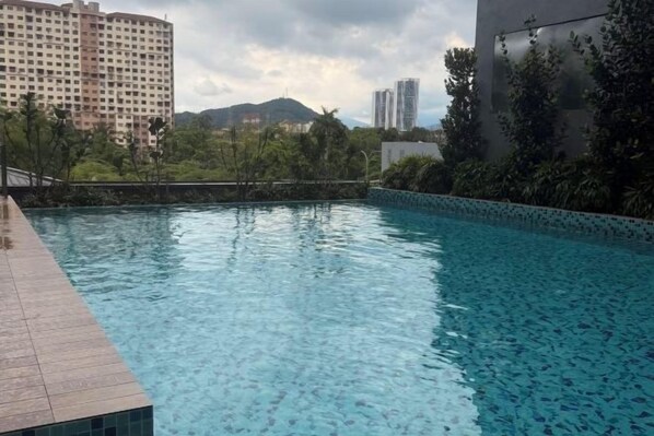 A swimming pool with a tiled edge, surrounded by greenery and buildings in the background.