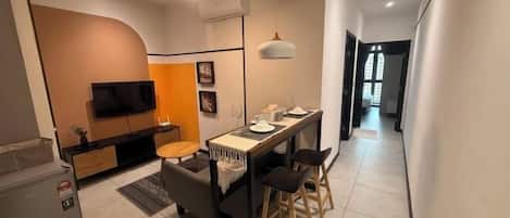 A modern kitchen with a built-in oven, a dining area with a table and chairs, and a TV mounted on the wall.